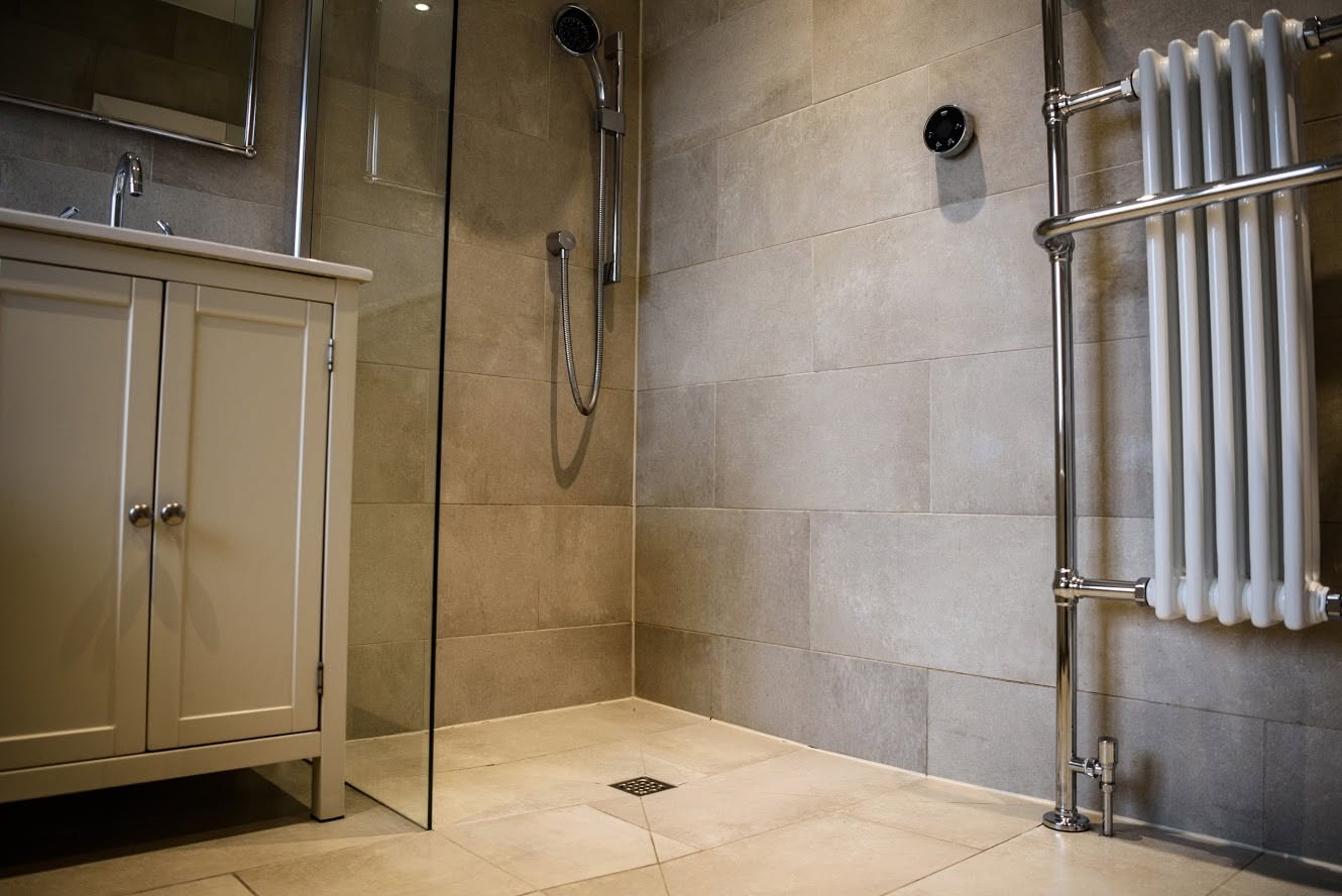 A walk-in shower with a glass screen, a grey vanity unit and a traditional column towel radiator