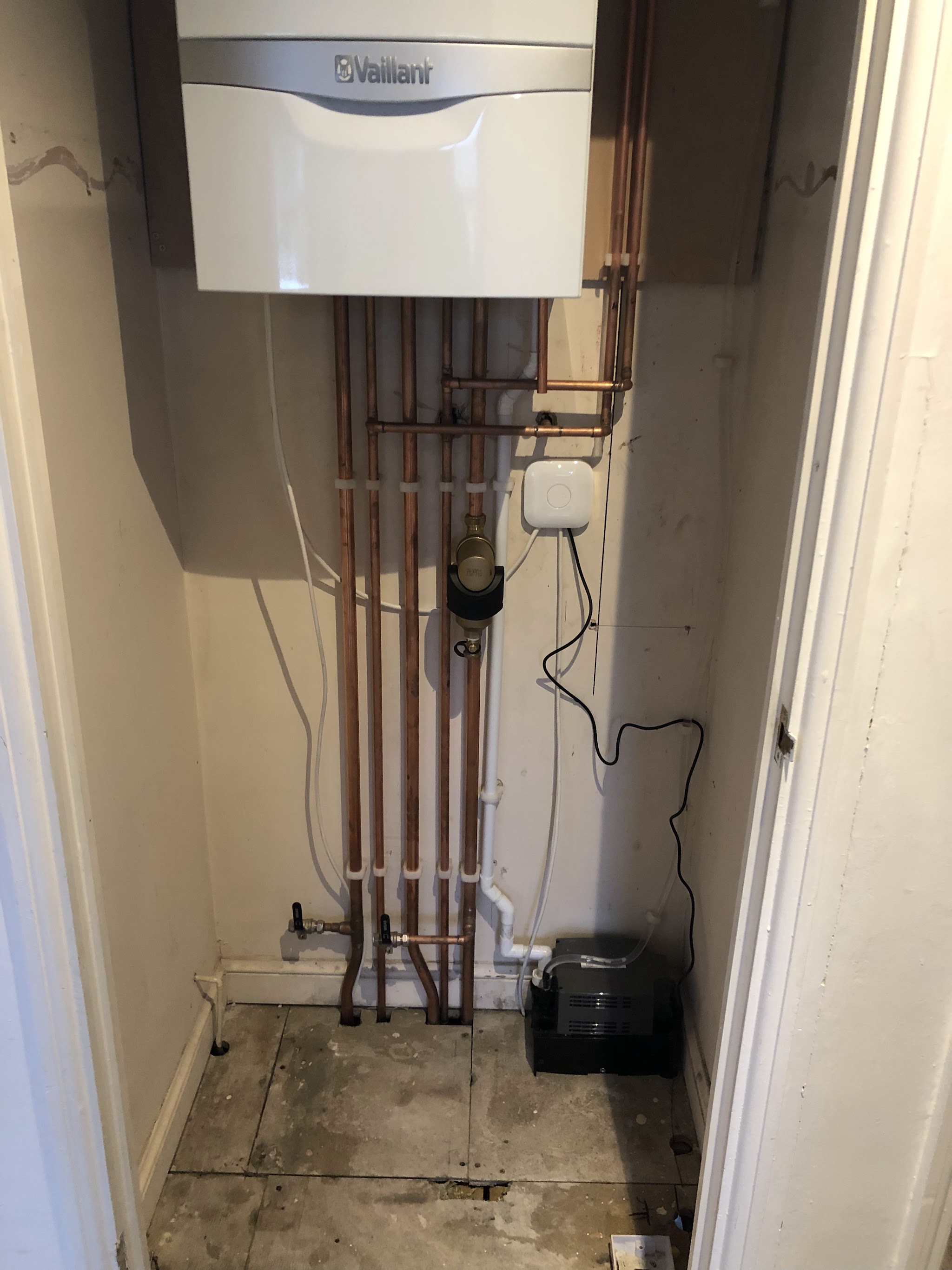 A white Vaillant boiler in a cupboard with copper flow and return pipes and a filter beneath it