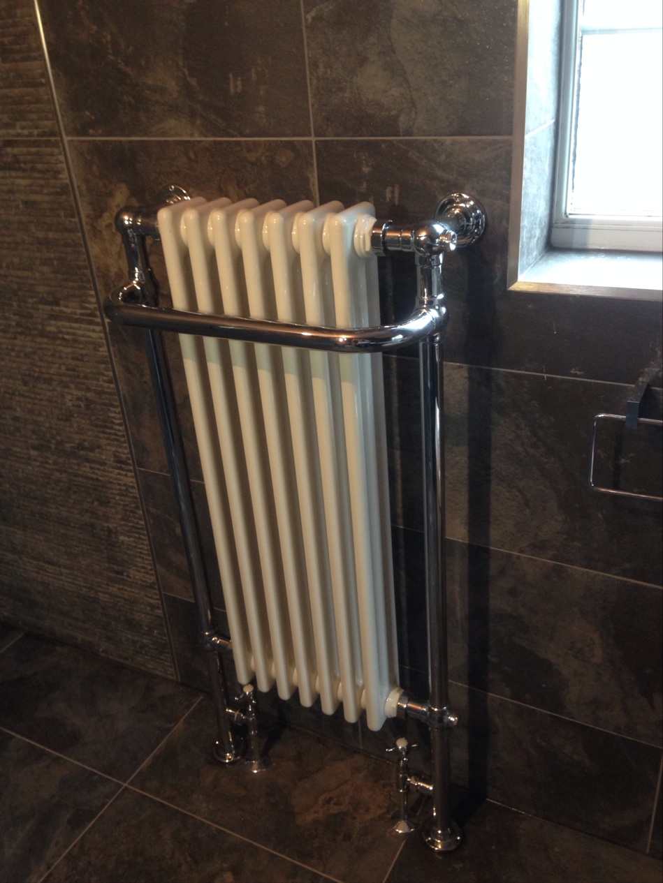 A chrome traditional column towel radiator on a dark slate tiled bathroom wall
