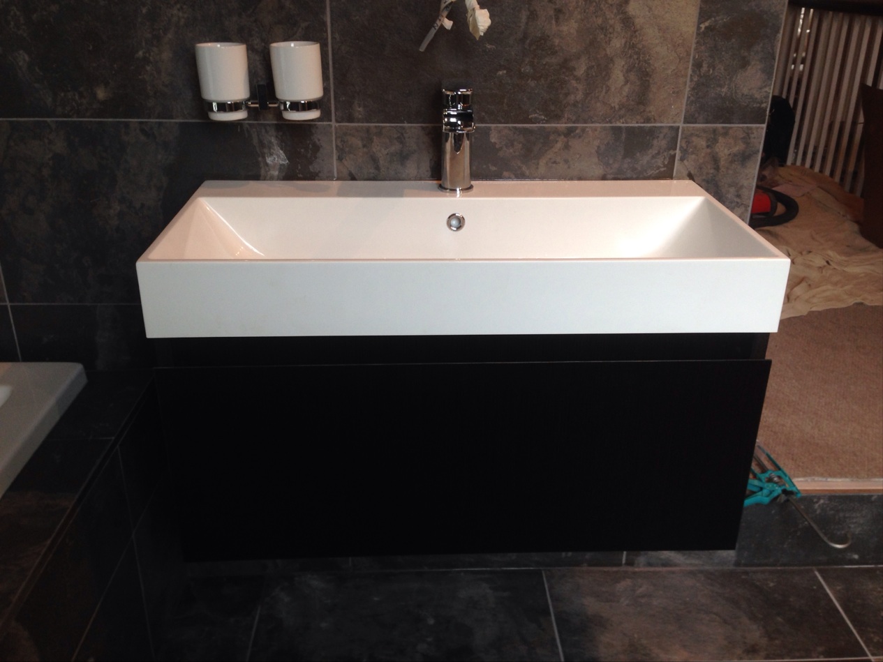 A white rectangular basin on a black vanity unit in a dark tiled bathroom